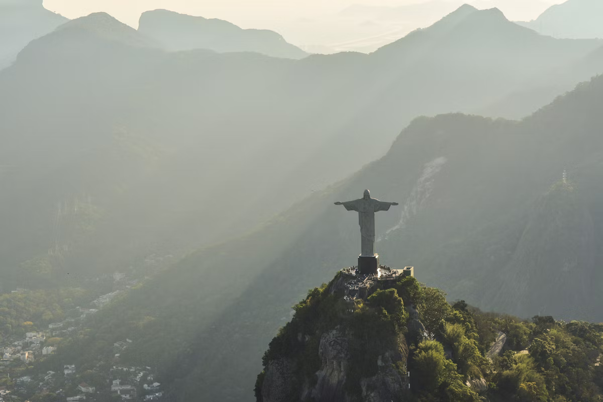 Aerial view of the Christ the Redeemer statue overlooking Rio de Janeiro, surrounded by misty mountains at sunrise.