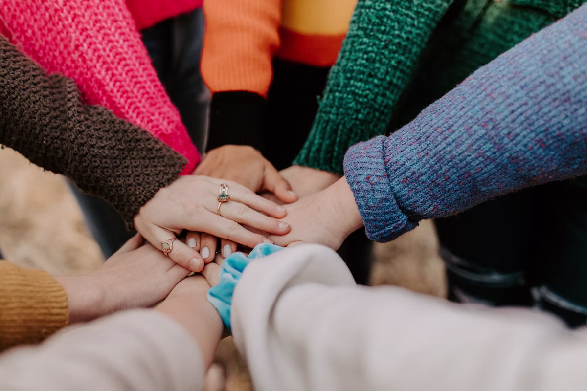 A group of people stacking their hands together to symbolize teamwork, unity, and community support.